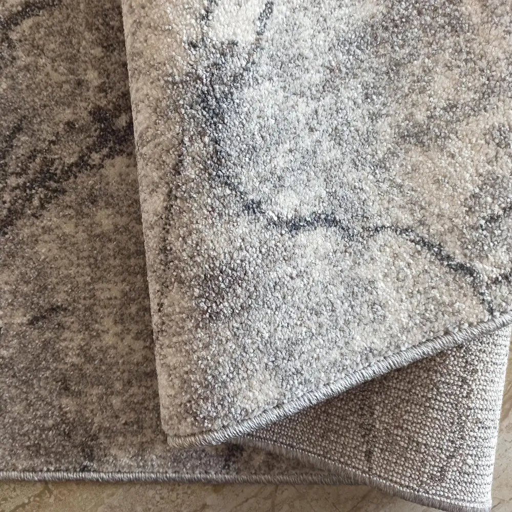 Tepe Vista 08 grått teppe, nærbilde av marmormønster og brettet hjørne som viser tekstur og underside.