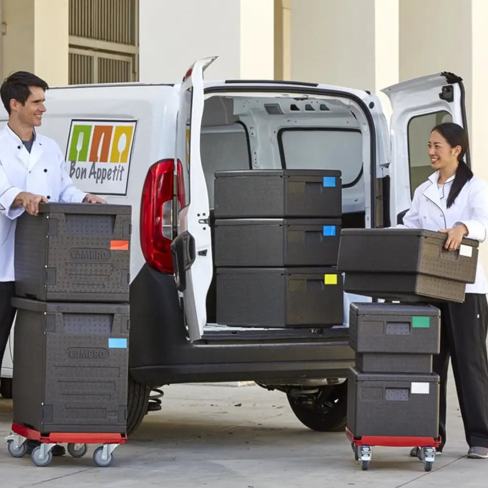 Termisk isolert beholder med frontmatning, stablet på rød tralle, flyttes av to kokker fra varebil.