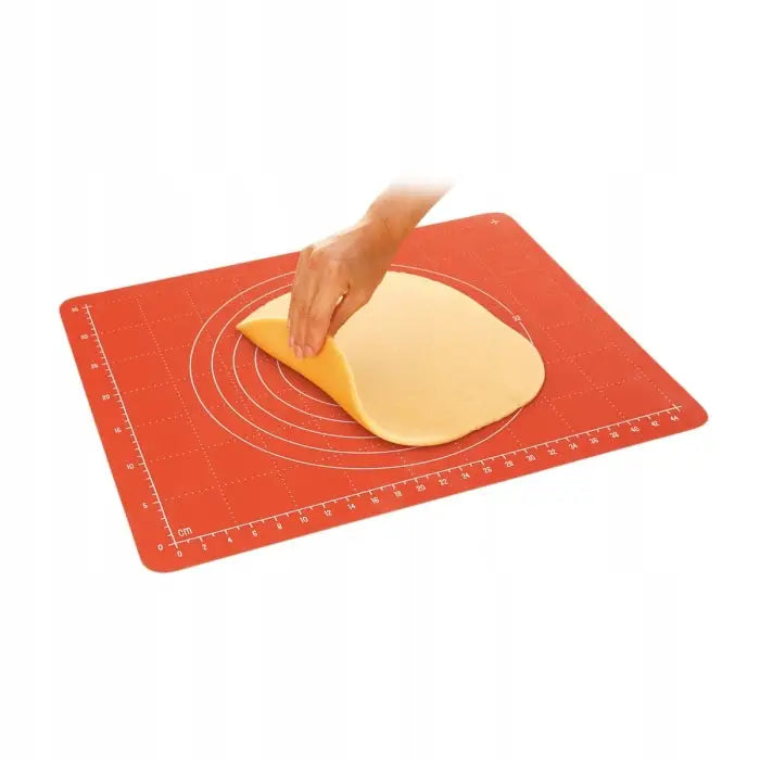 Tescoma bakematte i rød silikon med hvite mål, hånd løfter tynn deig fra matten på hvit bakgrunn.