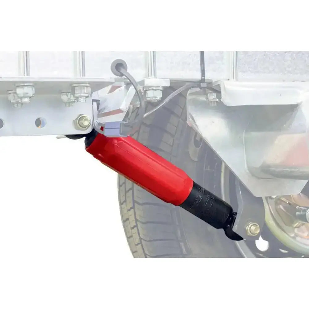 Tilhengeraksel støtdemper AL-KO i rødt og svart, sidevisning montert på tilhenger med hjul og ramme bak.