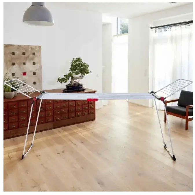 Tørkestativ for klær XXL Vileda Infinity 3M, sidevisning i lys stue med røde plastdetaljer på metallrammen.