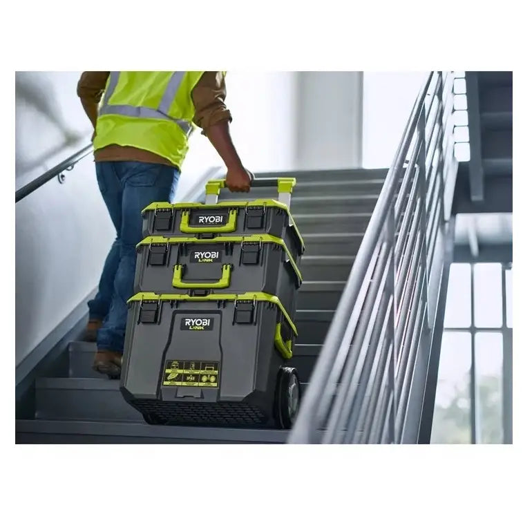 Transporttralle På Hjul Ryobi med tre grå verktøykasser og grønne detaljer trilles opp en trapp av en person.