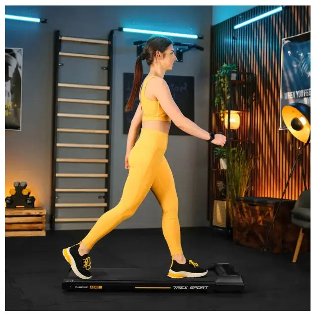 Tredemølle for hjemmetrening AERO Trex Sport, kvinne går på sort lavprofil løpebånd i stilrent treningsrom.