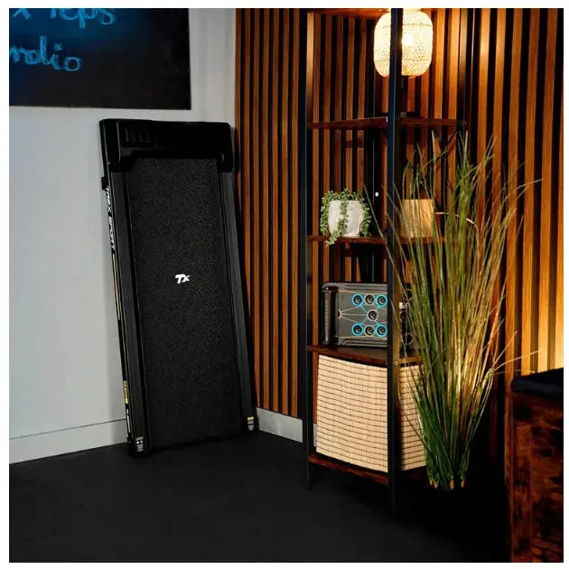 Tredemølle for hjemmetrening, sammenlagt sort modell stående mot vegg i moderne rom med trepanel.