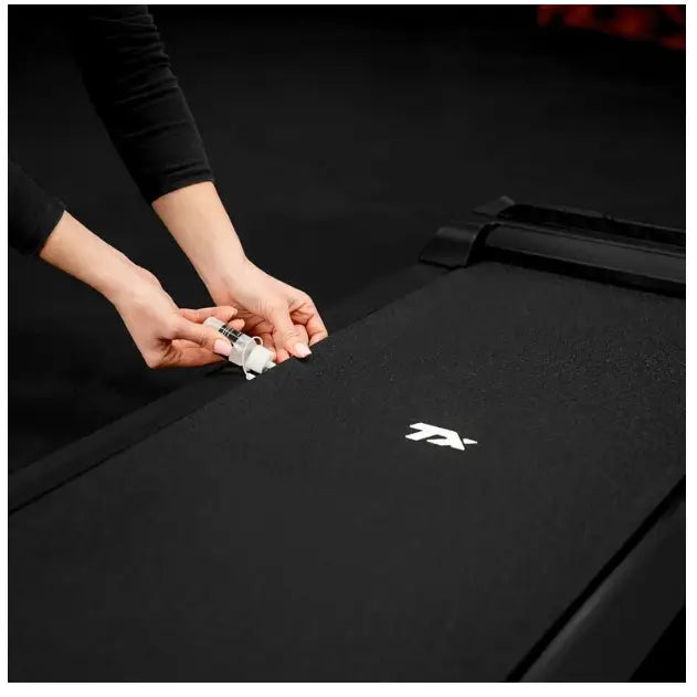 Tredemølle for hjemmetrening, nærbilde av to hender som rengjør det svarte båndet med hvit logo.