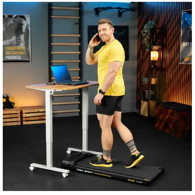 Tredemølle for hjemmetrening, sidevisning med en mann som går foran hevbart skrivebord med PC.