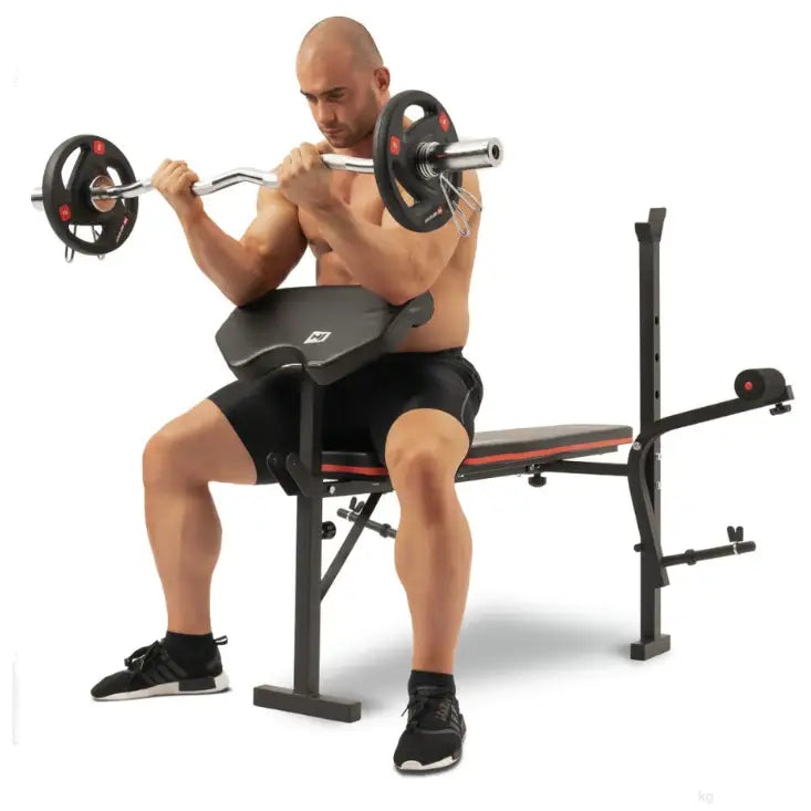 Treningsbenk med vektstangsett, sidevisning der en person gjør bicepscurl med armstøtte og stang.