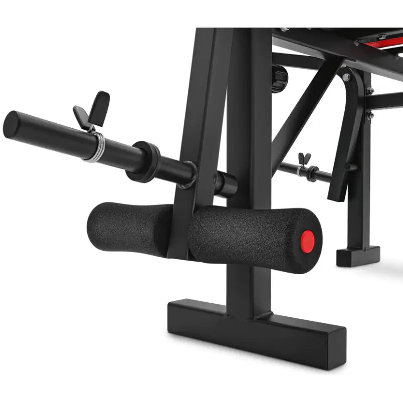 Treningsbenk med vektstangsett, nærbilde av polstret fotstøtte med rødt endestykke og låsemekanisme.