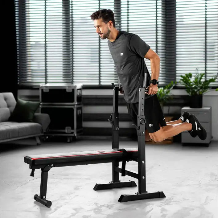 Treningsbenk med vektstangsett, sidebilde hvor en person utfører dips på stativet, røde detaljer synlige.