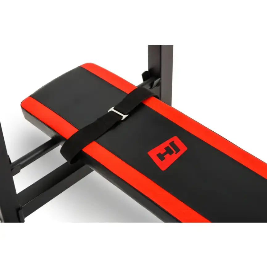 Treningsbenk med svarte og røde kunstskinnpolstringer, skrå vinkel, fokus på stropp med metallspenne.