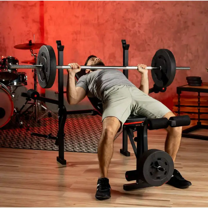 Treningsbenk med vektstangsett, mann utfører benkpress, skrå forfra med vektskiver og treningsutstyr i bakgrunnen.