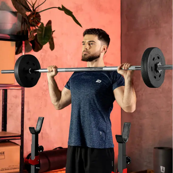 Treningsbenk med vektstangsett, mann løfter svarte vektskiver i hjemmegym mot rød bakgrunn, frontvisning.