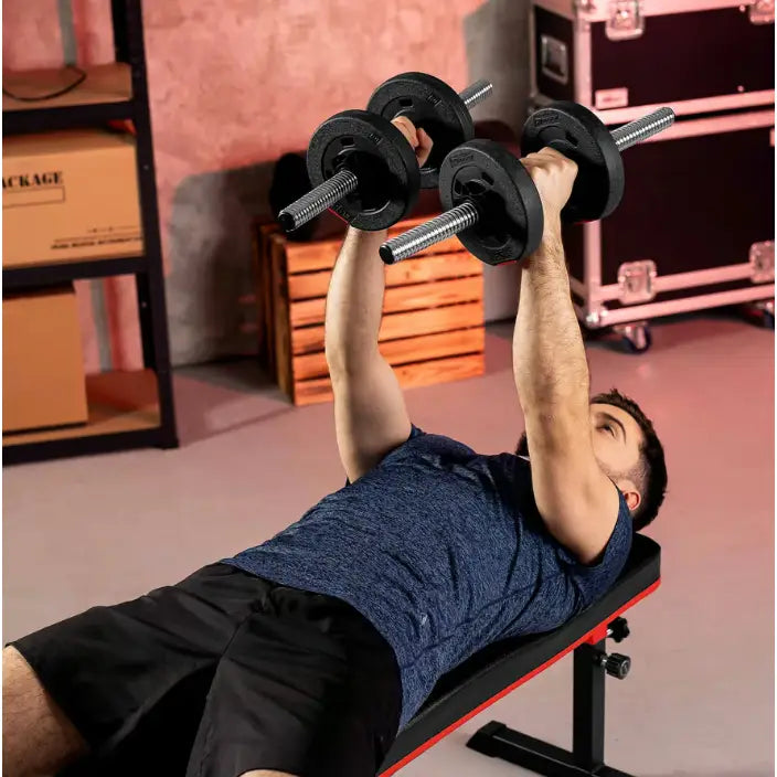 Treningsbenk med vektstangsett, mann løfter stålfargede manualer, sidevisning med treningsutstyr i bakgrunnen.