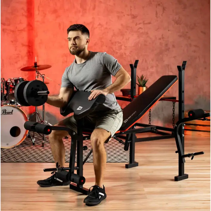 Treningsbenk med vektstangsett, mann løfter manual på svart og rød benk med polstrede puter, skrå vinkel.