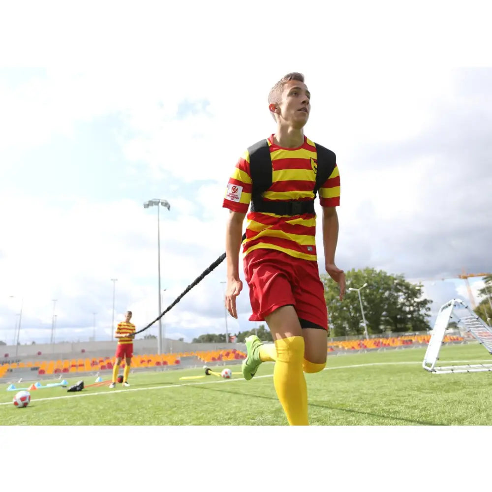 Treningshastighetsgummi i bruk, ungdom løper på kunstgress med svart motstandsbånd og sele festet til midjen.