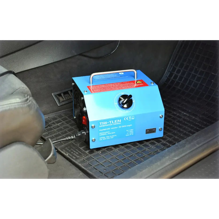 Tri-Tlen ozongenerator, blå modell med håndtak og ratt, i bruk på gulvmatte inne i bilens kupé.