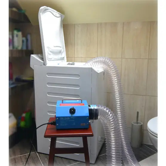 Tri-Tlen ozongenerator, blå modell med plastslange, står på stol foran åpen hvit vaskemaskin.
