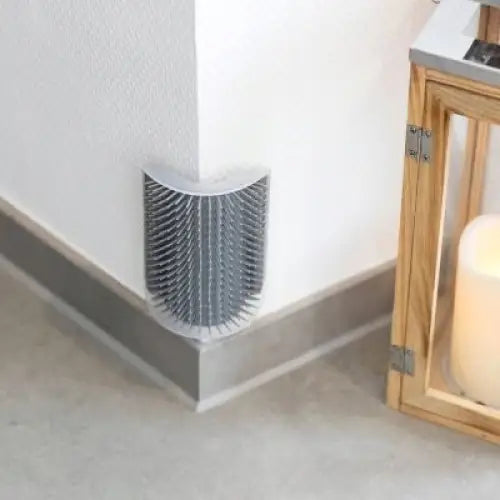 Trixie hjørnebørste for katter 8x13 cm grå, festet i et hjørne mot hvit vegg og tregulv, med tette plastbust.