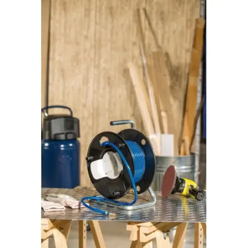 Trykkslange på kabeltrommel, blå ledning og svart ramme, plassert på arbeidsbord i aktivt verksted.