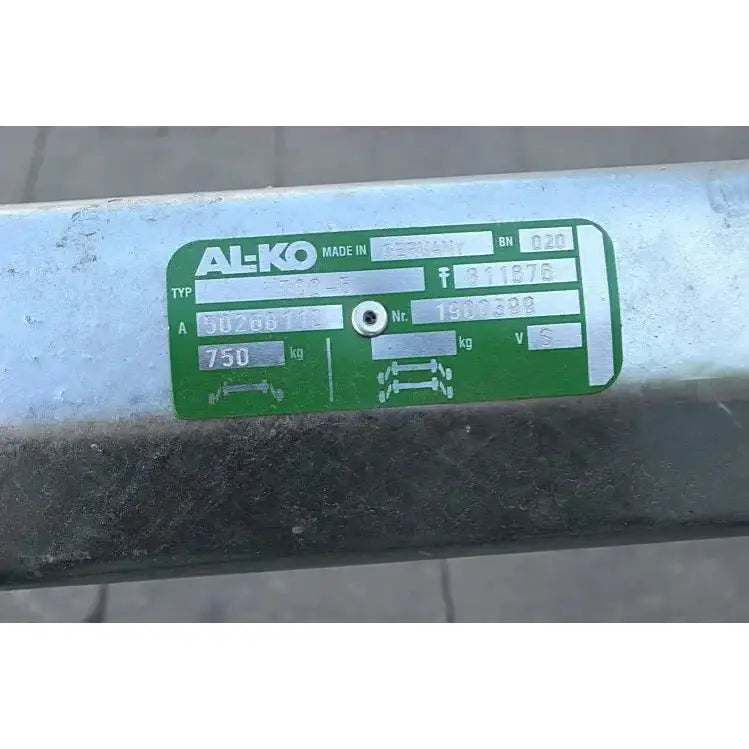 Aksling for tilhenger med grønt og sølvfarget merkeskilt, nærbilde av tekniske spesifikasjoner på metall.