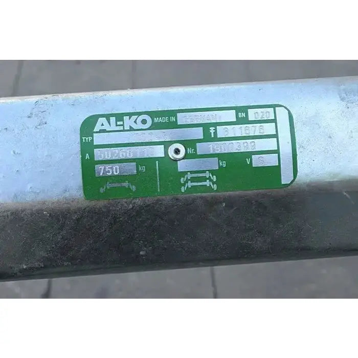 Aksling tilhenger AL-KO med grønt og hvitt informasjonsskilt, nærbilde av tekniske spesifikasjoner på metallrøret.