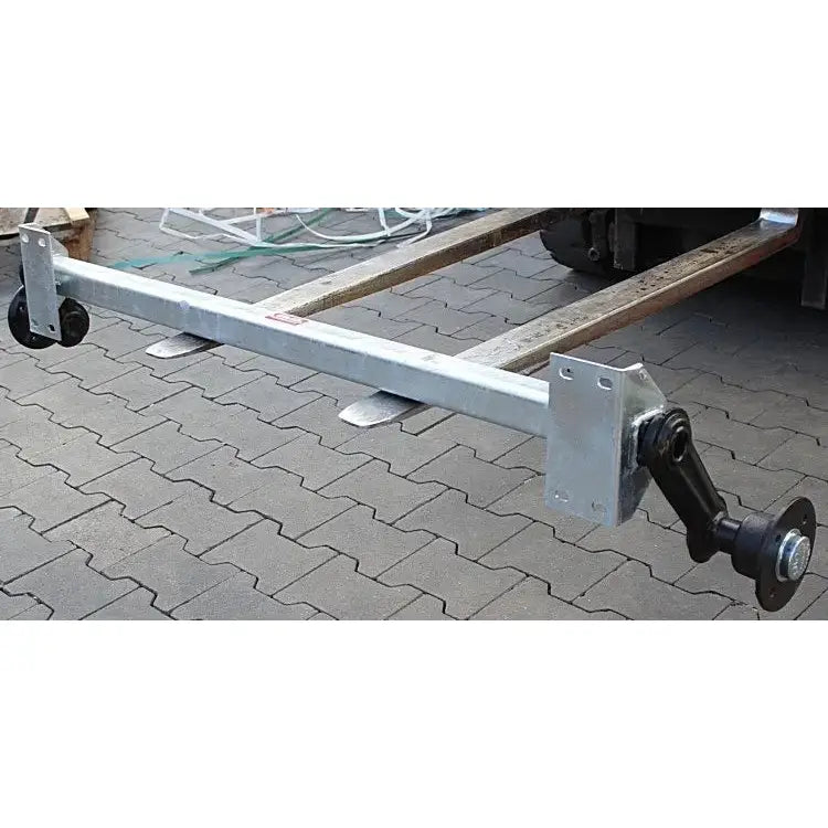 Aksling for tilhenger Knott VG7-L, sett fra siden med hjul og sort koblingspunkt på brosteinsbakke.