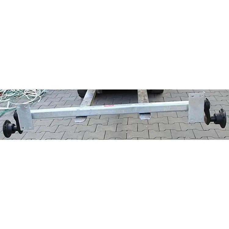 Aksling tilhenger Knott VG7-L, frontvisning av galvanisert stålaksel med sorte nav på belegningsstein.