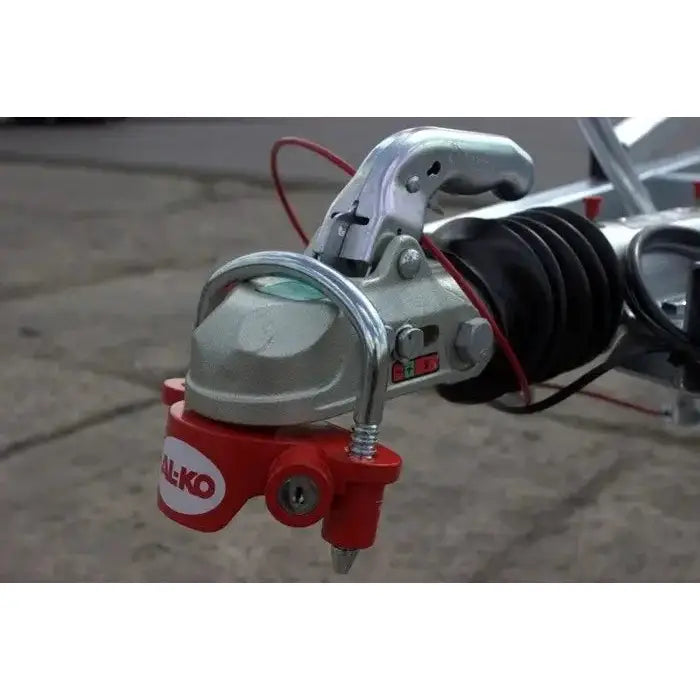 UniversalfestelÄs for tilhengere fra AL-KO, rÞdt lÄs montert pÄ sÞlvfarget kobling med synlig sikkerhetswire.