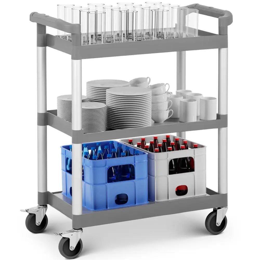 Universell vogn med tre grå plast-hyller, fylt med glass, servise og plastkasser med flasker, sett fra siden.