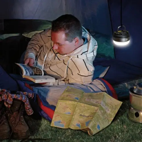 Utendørslampe LED, brukt som hodelykt i telt mens en mann leser, med kart og fjellstøvler i forgrunnen.
