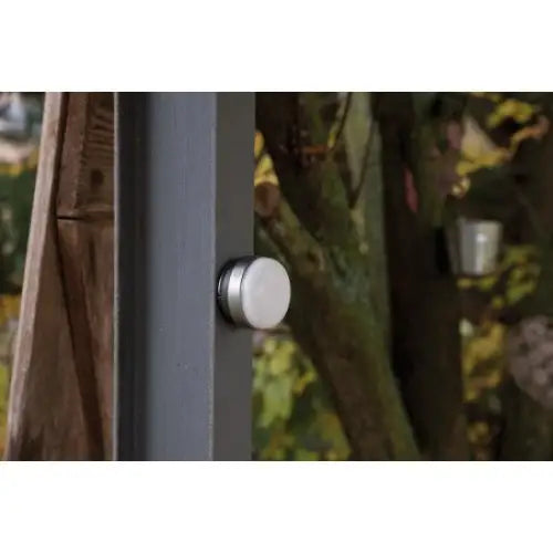 Utendørslampe LED OLI, sølvfarget sensor på mørk stolpe fotografert fra siden mot grønn bakgrunn.