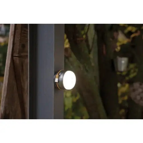 Utendørslampe LED, sidevisning av sølvfarget rund modell med hvit front montert på mørk vegg utendørs.