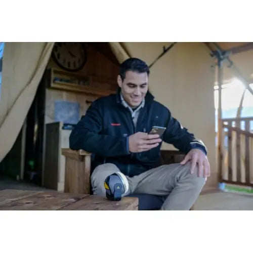 Utendørslampe LED OLI 310 AB med høyttaler, brukt i telt, mann sitter og ser på mobil, sko med gule detaljer.