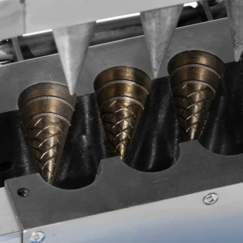 Vaffeljern for iskremkjeks, nærbilde av tre koniske former under metalltrakter i produksjonsmaskin.