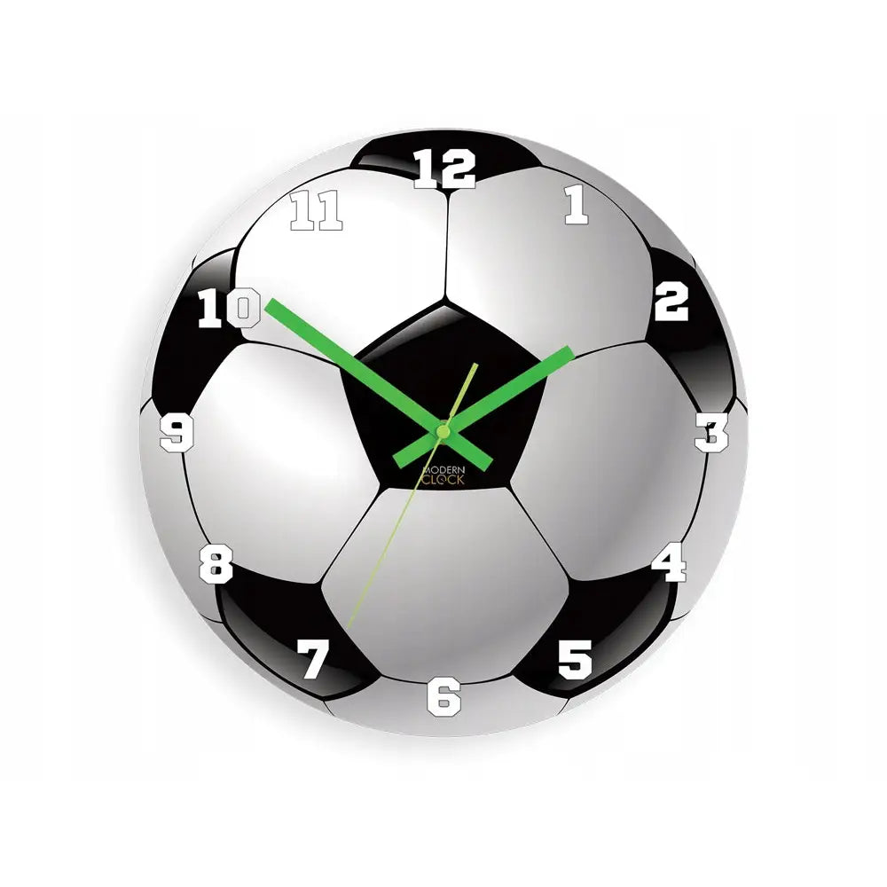 Veggklokke formet som en sort og hvit fotball, grønne visere og store hvite tall, frontvisning mot hvit bakgrunn.