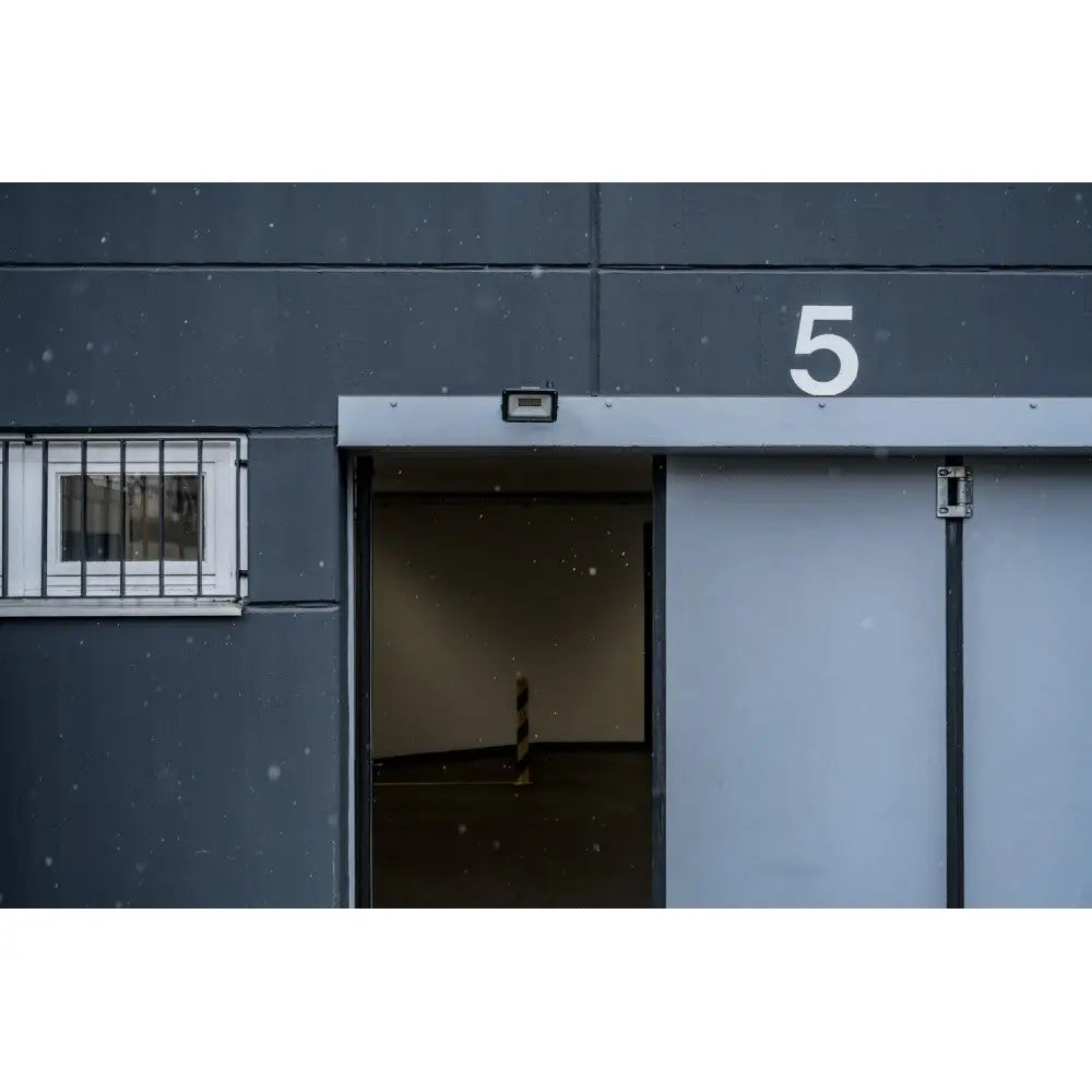 Mørk grå garasjeport med hvitt tall 5, delvis åpen, snøfnugg foran og vindu med gitter til venstre.