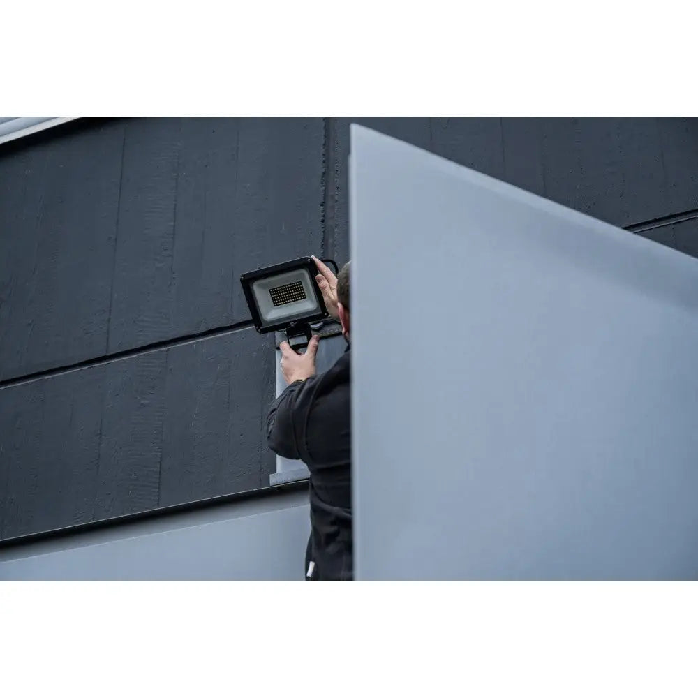 Vegglampe LED JARO 7060 P monteres på mørk yttervegg, fokus på installasjon og armaturens sorte design.