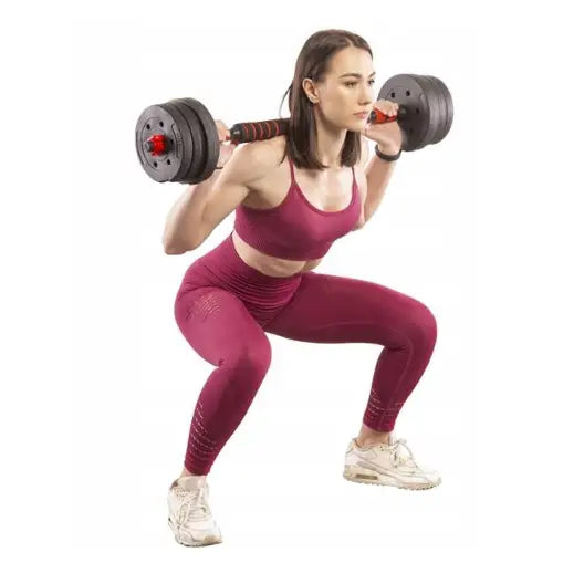 Vektsett med stang og hantler, kvinne i rødt treningstøy gjør knebøy med svart og rød stang, sideprofil.