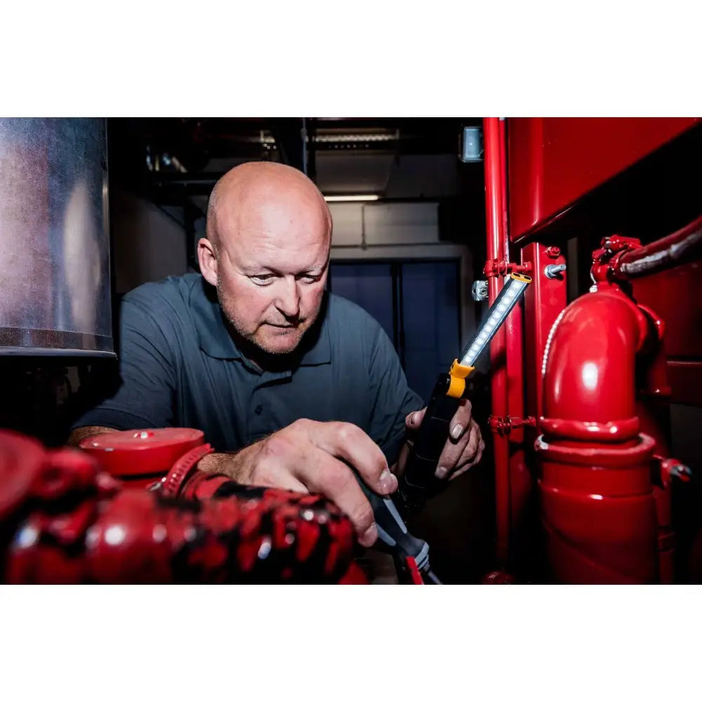 Verkstedlampe LED SANSA 400A i bruk, holdt av en mann blant røde rør og tekniske installasjoner.