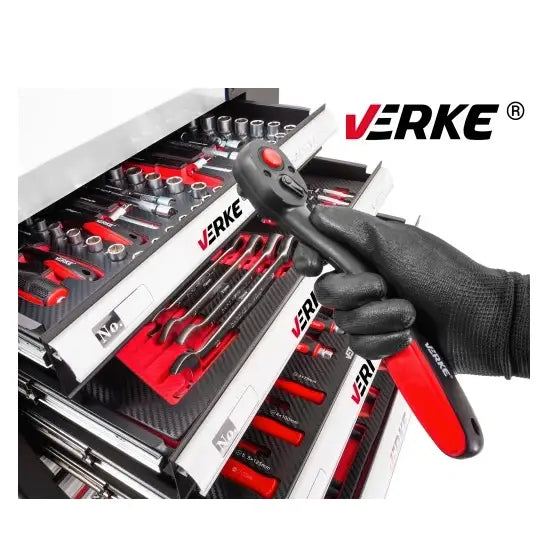 Verkstedsvogn med verktøy, hanskekledd hånd holder sort og rød skralle foran åpne skuffer med håndverktøy.