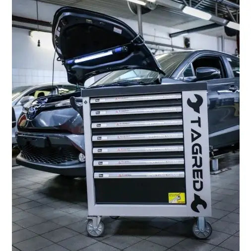 Verkstedvogn Tagred, grå med syv skuffer og store hjul, plassert ved bil med åpent panser i verksted.
