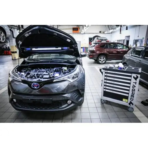 Verkstedvogn Tagred med verktøy, plassert ved en grå bil med åpent panser i et moderne verkstedmiljø.