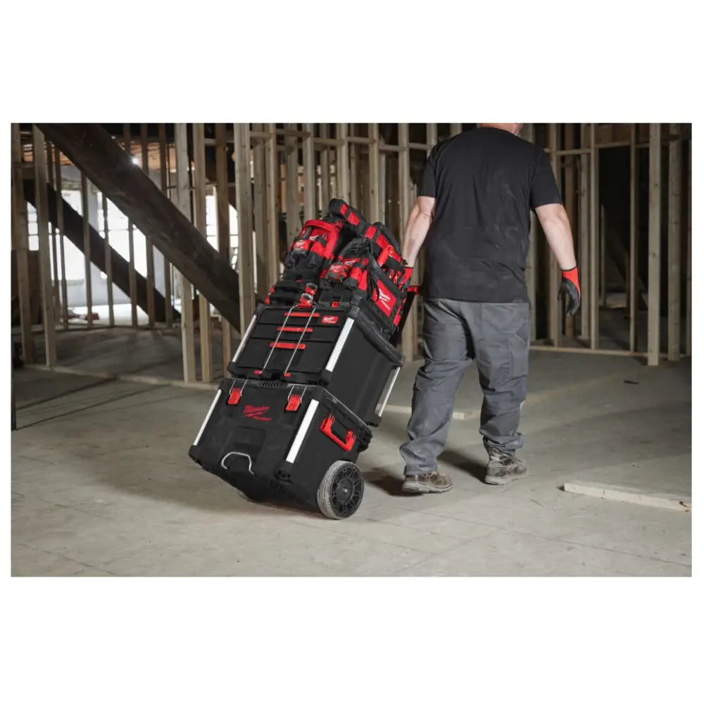 Milwaukee Packout verktøykasse med skuffer, trilles på hjul av en person gjennom byggeplass med rå trevegger.