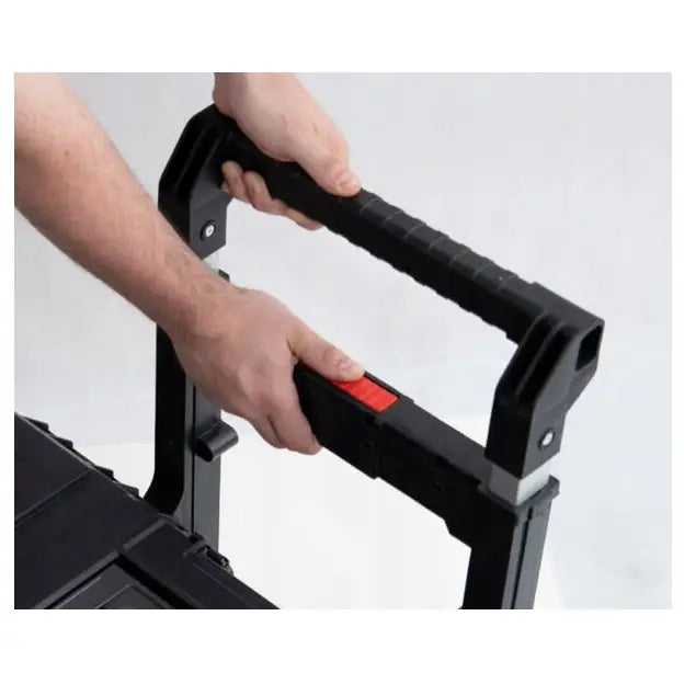 Verktøykasse Qbrick One Cart 20, sort teleskophåndtak med rød låseknapp holdes av to hender, skrå vinkel.