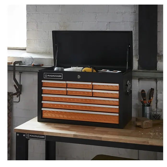 Verktøyskap Magnusson med 9 skuffer, åpent lokk og synlige vernebriller foran oransje skuffefronter.