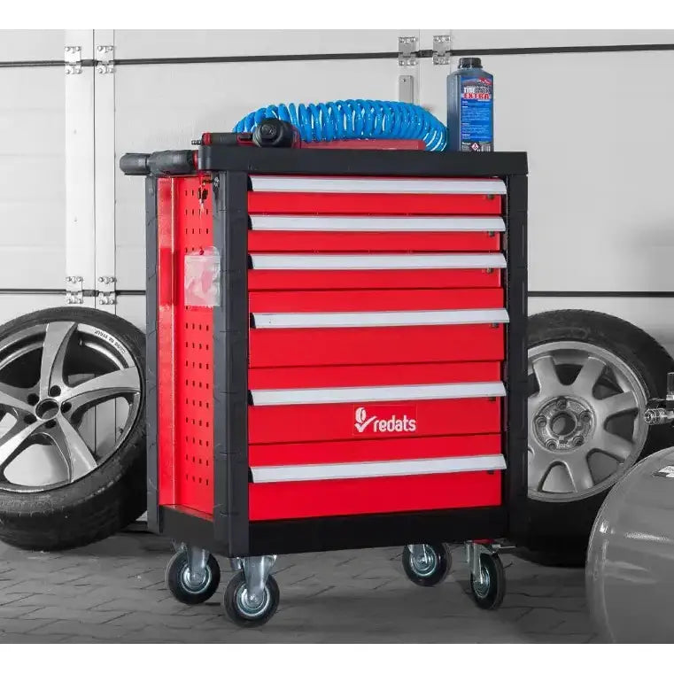 Rød verktøyvogn i metall med flere skuffer, sett forfra fra siden, slange og flaske på toppen, på hjul.