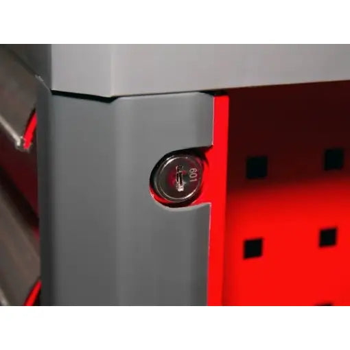 Verktøyvogn Proline, nærbilde av grå metallkant med låsesylinder mot rød perforert bakgrunn.