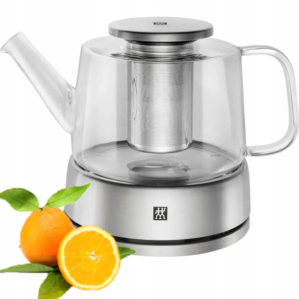 Zwilling glass tekanne med metallinfuser og lokk, stålfarget base, appelsin med blad ved siden av.