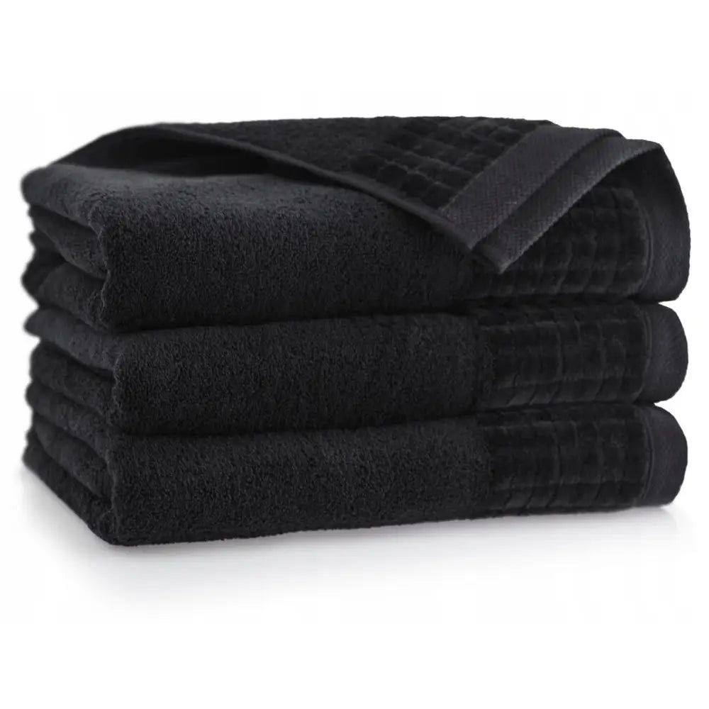 Zwoltex svarte bomullshåndklær med rutemønstret kant, stablet fra siden mot hvit bakgrunn.