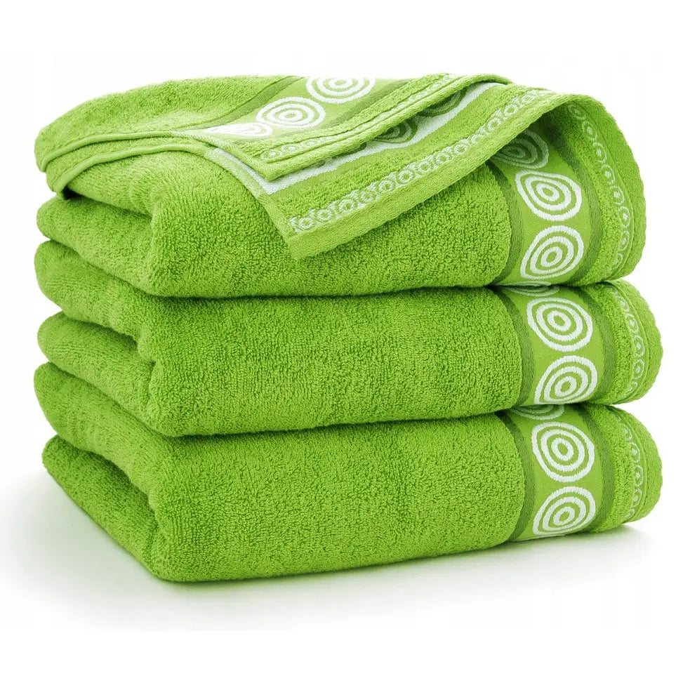 Zwoltex grønne håndklær i frotté, tre størrelser pent stablet med dekorative hvite sirkler langs kanten.